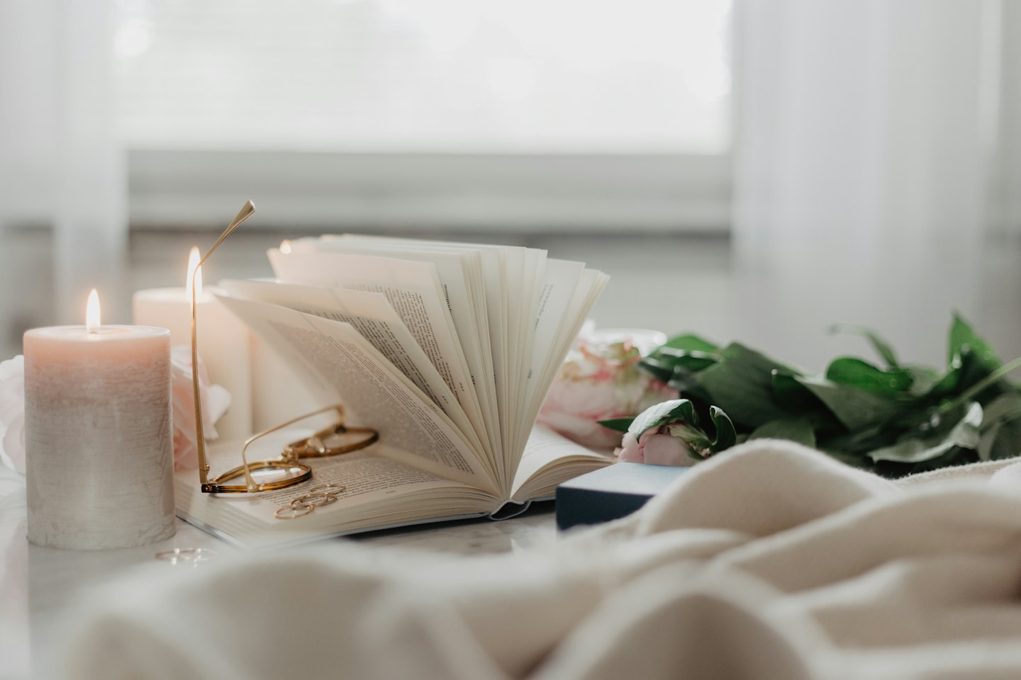 Libro aperto con occhiali da lettura e candele su una coperta.